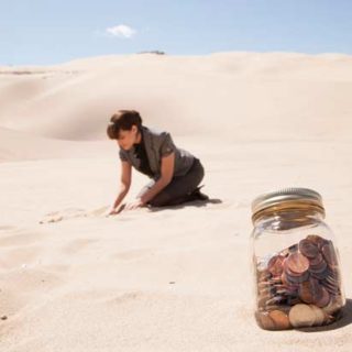coin jar in the sand and woman is digging in the background