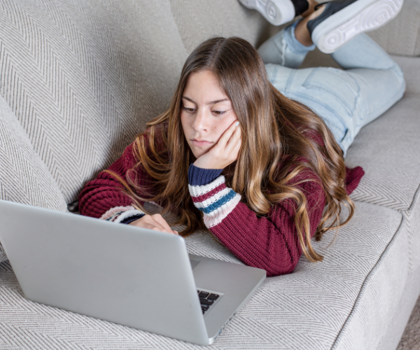 Teen girl lays on couch with computer laptop